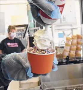  ??  ?? Curry Freeze owner Bob Draiss adds whipped cream to a cup of soft serve ice cream as Mimi Burdo handles the cash at the window.