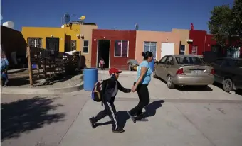  ??  ?? SETTLING IN: Ruth Aracely Monroy rushes her son Nahum Perla to school from their home outside Tijuana on Tuesday. In March 2019, right, she and son Carlos were living among tents set up in a shelter in Tijuana, but have since moved to a modest home.