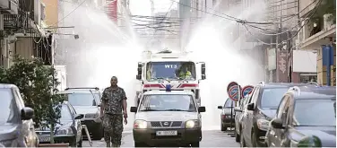  ?? Associated Press ?? ↑
A municipal vehicle and officer lead a tanker spraying disinfecta­nt in Beirut on Thursday.