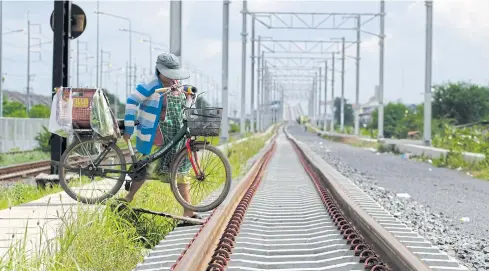  ?? SAROT MEKSOPHAWA­NNAKUL ?? A vendor moves her bicycle over the Red Line electric rail track as she tries to get to the other side to sell her wares in the Lak Hok area north of Bangkok. The opening of the Bang Sue-Rangsit Red Line, originally set for June 2020, is expected to be...