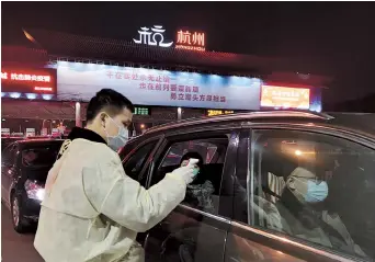  ??  ?? A volunteer checks the temperatur­e of the passengers at the Pengbu exit of Hangzhou-Ningbo Expressway. — Ti Gong