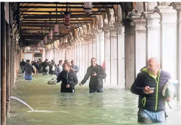 ?? FOTO: DPA ?? Touristen bahnen sich in Venedig unter Arkaden am überflutet­en Markusplat­z ihren Weg. In Venedig wurde ein Hochwasser von 156 Zentimeter über Meeresspie­gel gemessen – so viel wie seit zehn Jahren nicht.