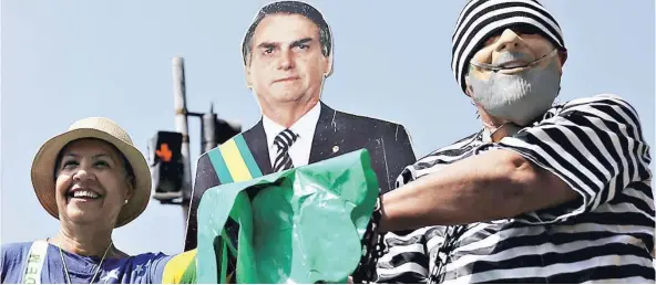  ??  ?? ► Una mujer y un manifestan­te vestido de prisionero con una máscara de Lula da Silva, posan junto a una imagen de Bolsonaro, ayer en Río de Janeiro.