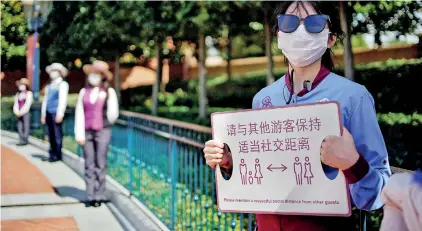  ?? ?? A staff member holds a sign reminding visitors to maintain social distance at the Shanghai Disney Resort, in Shanghai. (Reuters)