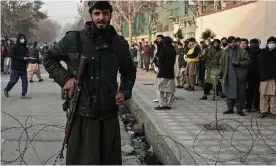  ?? Photograph: Mohd Rasfan/AFP/Getty Images ?? A Taliban fighter stands guard at a checkpoint as people queue to enter the passport office in Kabul on Sunday.