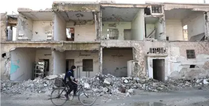  ?? —AFP ?? DOUMA, Syria: A Syrian man rides a bicycle past destroyed buildings in this rebel-held town on the eastern outskirts of the capital Damascus yesterday.