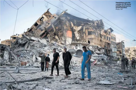  ?? Photo / AP ?? Palestinia­ns pass the remains of a 15-storey building destroyed by Israeli airstrikes.