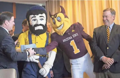  ?? PATRICK BREEN/THE REPUBLIC ?? Gov. Doug Ducey shakes Sparky's hand during his signing of a $1 billion university bill. Louie the Lumberjack and Michael Crow flank Sparky.