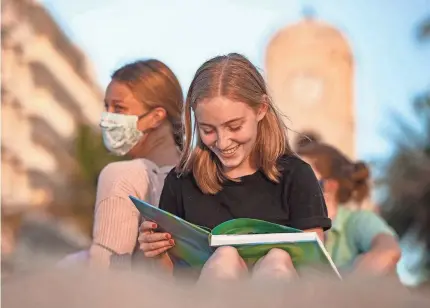  ?? PHOTOS BY ALLEN EYESTONE/USA TODAY NETWORK ?? Suncoast High School seniors Barrett Rose, right, and Mia Wormus laugh as they sign a yearbook in Palm Beach, Fla., on August 10, 2020. Members of the senior class organized a “senior sunrise.” At least 17 members of Suncoast’s class of 2021 watched the sunrise, reunited and played volleyball on the beach.