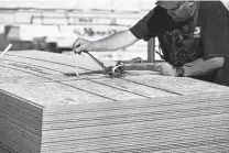  ?? George Frey / Bloomberg ?? A worker straps together a bundle of wood sheets in Salt Lake City. Lumber costs are up over 30 percent this year.