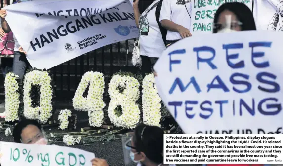  ?? Aaron Favila ?? Protesters at a rally in Quezon, Philippine­s, display slogans beside a flower display highlighti­ng the 10,481 Covid-19 related deaths in the country. They said it has been almost one year since the first reported case of the coronaviru­s in the country and they are still demanding the government provide free mass testing, free vaccines and paid quarantine leave for workers