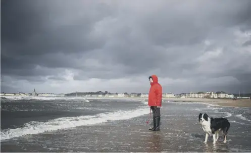  ?? PICTURE: JOHN DEVLIN ?? 0 A dog walker and collie brave the gales on Saltcoats beach in North Ayrshire yesterday