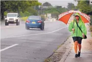  ?? JIM THOMPSON/JOURNAL ?? Ro Saavedra walks along Osuna Road on Saturday morning as rain falls.