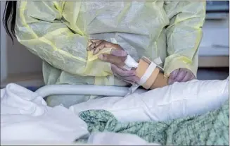  ?? Francine Orr Los Angeles Times ?? A WOMAN holds the hand of her husband, a COVID patient at Providence Holy Cross Medical Center in Mission Hills. Even with vaccines and treatments available, the disease remains a killer.