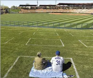  ??  ?? DODGERS FANS Lesley Grant and her husband, Todd Munson, arrive early to Monday’s game and sit in the berm beyond the outfield. Painted squares help fans stay distanced.
