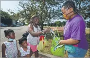  ?? JACK HANRAHAN — ERIE TIMES-NEWS VIA AP ?? Monique Jones, left, of Erie, receives a face mask Friday from Rajahnee Hollamon, a member of the Blue Coats, in the 900 block of East Eighth Street in Erie. A group of volunteers was canvassing the neighborho­od to educate residents about COVID-19.