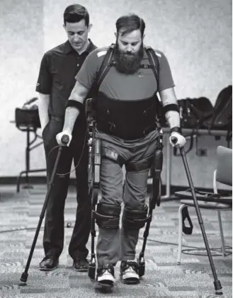  ??  ?? Army Sgt. Dan Rose, assisted by Mike Glover, tries out the exoskeleto­n suit at the Department of Veterans Affairs medical center in Denver on Wednesday. Kenneth D. Lyons, The Denver Post