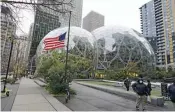  ?? — AP ?? A US flag flies in front of the Amazon Spheres on the company’s corporate campus in Seattle. Amazon Web Services suffered a major outage on Tuesday.