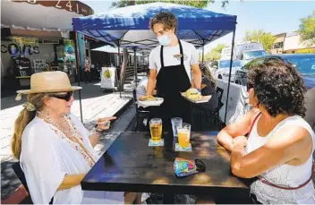  ?? CHARLIE NEUMAN ?? Ben Siemens serves Martina Foss (left) and friend Lilia Beeson in front of Burger Bench on Grand Avenue.