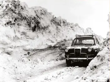  ?? ?? A car manages to navigate a path cleared by a bulldozer near Crediton, Devon, in 1963. The Big Freeze hit hard in the South West, with snowdrifts reaching more than six metres in height. Helicopter­s had to be used to reach some isolated homes.