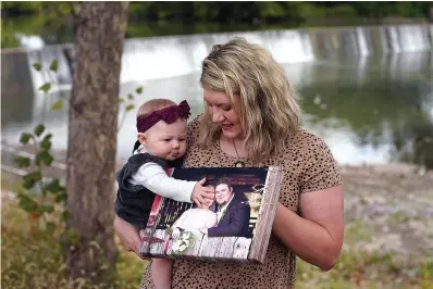  ?? The Associated Press ?? ■ Aubrea Baker displays her wedding photo as she and her 7-month-old daughter Haylen visit one of her late husband’s favorite fishing spots Saturday in Burlington, Kan. Her husband, Danny Baker, was among the 700,000 U.S. victims of COVID-19, dying on Sept. 14 after testing positive in July.