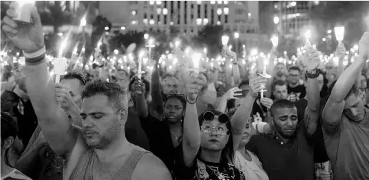  ?? IMAGES DREW ANGERER/GETTY ?? People hold candles during an evening memorial service for the victims of the Pulse Nightclub shooting at the Dr. Phillips Center for the Performing Arts on June 13, 2016.
