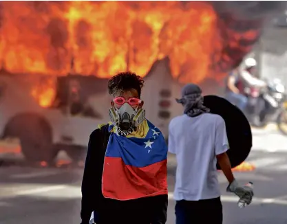  ?? —REUTERS ?? CARACAS BURNING Demonstrat­ors stand next to a burning bus near the site of protest rallies against Venezuelan President Nicolas Maduro.