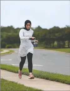  ?? (AP/Jessie Wardarski) ?? Amirah Ahmed, 17, checks her watch while running near her home in Fredericks­burg, Va.