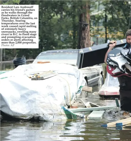  ?? Photo: AP ?? Resident Lars Androsoff carries his friend's guitars as he walks through the floodwater­s in Grand Forks, British Columbia, on Thursday. Soaring temperatur­es over the last week caused rapid melting of extremely heavy snowpacks, swelling many rivers in...