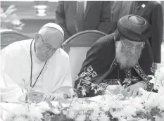  ?? AGENCE FRANCE PRESSE ?? This handout picture released by the Vatican press office shows Pope Francis and Pope Tawadros II, spiritual leader of Egypt's Orthodox Christians, signing a joint declaratio­n pledging to "strive for serenity and concord through a peaceful co-existence...