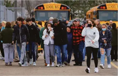  ?? Eric Seals / Detroit Free Press ?? Parents walk away with their kids from a Meijer grocery store parking lot, where many students gathered after a shooting at Oxford High School in Oxford, Mich. The suspected shooter was taken into custody.