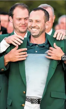  ??  ?? Defending Masters champion Danny Willett places the jacket on Sergio Garcia on Sunday at Augusta National Golf Club.