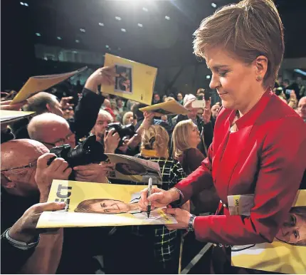  ?? Pictures: PA. ?? Above: Nicola Sturgeon signs copies of the SNP’s manifesto. Right: the SNP leader addressing the gathering as supporters hold up copies of the manifesto.