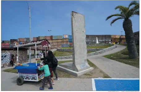  ?? GREGORY BULL — THE ASSOCIATED PRESS ?? A family pushes a snack cart past a slab of the Berlinwall, displayed near the borderwall that separates the United States frommexico, in Tijuana, Mexico, Friday, Aug. 25, 2023. The 3-ton pockmarked, gray concrete slab sits between a bullring, a lighthouse and the borderwall, which extends into the Pacific Ocean.