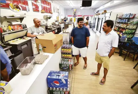  ?? Christian Abraham / Hearst Connecticu­t Media ?? Sam Chidella, at right, stops by Mama Carmela's Deli, where he likes to hang out in Darien. In center is Sam's son Phaneendra. Chidella, a manager at Darien Exxon Mobil for 25 years, is retiring and heading back to India, his home country.