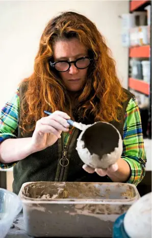  ??  ?? At her workbench, Siobhan Newton creates an earthy finish to one of her microcosms. She applies liquid clay to the outer surface, to ensure ground granite from the local landscape will successful­ly adhere to it.