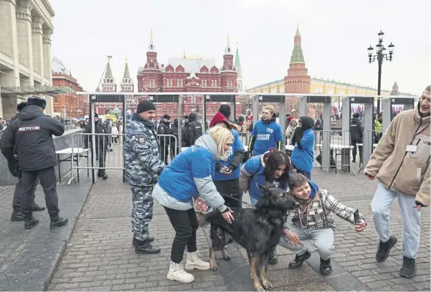  ?? ?? Volunteers take a selfie with a service dog in front of metal detectors as people arrive for a rally and a concert celebratin­g the tenth anniversar­y of Russia’s annexation of Crimea at Red Square, in Moscow