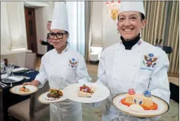  ?? ANDREW HARNIK — THE ASSOCIATED PRESS ?? White House Executive Chef Cris Comerford, left, and Executive Pastry Chef Susie Morrison hold dishes Wednesday during a preview for the state dinner at which President Joe Biden will host French President Emmanuel Macron at the White House on Thursday.
