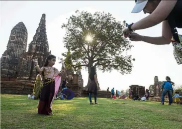  ?? —AFP ?? Say cheese: A Thai girl in traditiona­l costume posing for pictures at the ancient Wat Chaiwattha­naram temple in Ayutthaya province.