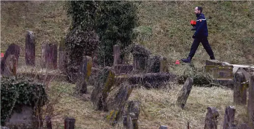  ?? (Vincent Kessler/Reuters) ?? A FRENCH GENDARME walks by some of 250 desecrated tombstones at the Sarre-Union Jewish cemetery, near Strasbourg, in this file photo.