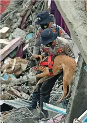  ?? (AFP) ?? A policeman carries his dog over the rubble during search operations for survivors underneath a collapsed hospital, in Mamuju on Sunday