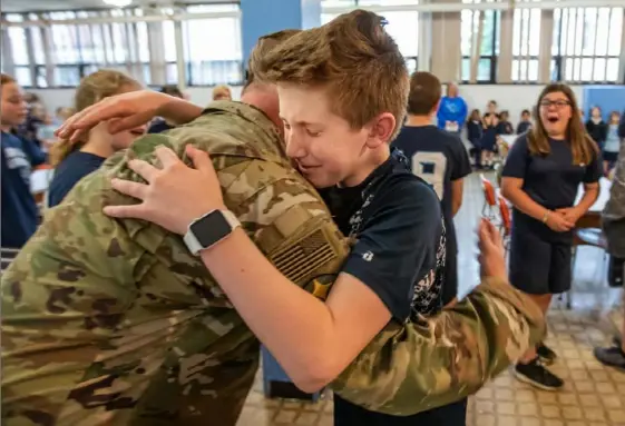  ?? Andrew Rush/Post-Gazette ?? Air National Guard Master Sgt. Patrick Gallagher hugs his surprised son Liam, 11, during an assembly Friday at Aquinas Academy in Greensburg. Liam and his brother, Connor, 18, who was also at the school as a volunteer for the assembly, did not know their father was coming. Sgt. Gallagher, who has nearly 30 years of service, was deployed for seven months to Afghanista­n and Guam. Story,