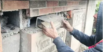  ??  ?? A worker removes a time capsule containing a Calgary Daily Herald newspaper from 1909. Crews discovered numerous items hidden away in a brick cornerston­e they were dismantlin­g.