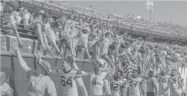  ??  ?? WEST Virginia players high-five fans after defeating Kansas, 38-22, in an NCAA college football game in Morgantown, West Virginia, in October 2018, as a fan washes his hands at a new disinfecti­on station in the stadium prior the German Bundesliga match between Borussia Dortmund and SC Freiburg in Dortmund, Germany, in Febraury.