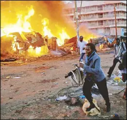  ?? REUTERS ?? People run past properties that were set on fire by rioters in the Kawangware slums in Nairobi on Friday.