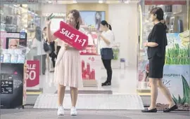  ?? Ed Jones AFP/Getty Images ?? A SALESWOMAN advertises at a cosmetics shop in Seoul. Many job seekers in South Korea doctor their head shots to make themselves look more attractive.