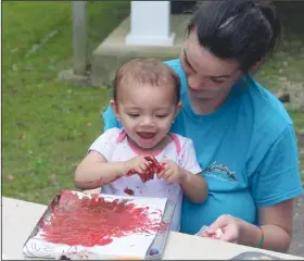  ?? Photos by Madeleine Leroux/News-Times ?? Magnets: Amber Easter holds her 16-month-old daughter, Mary, while she plays with paints during the National Kids to Park Day on Saturday at the Arkansas Museum of Natural Resources in Smackover. Below, Easter holds Mary while showing her how to use magnets and marbles to paint a picture.