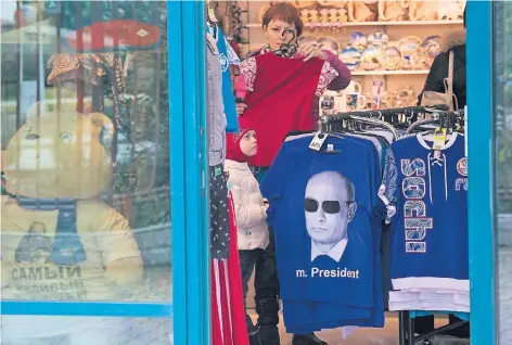  ?? FOTO: AP ?? T-Shirts mit Fotos von Wladimir Putin und patriotisc­her Nippes verkaufen sich gut in Sotschi, das seine erste Wintersais­on hinter sich hat. Mit Erfolg: Zeitweilig mussten wegen des Andrangs die Pisten gesperrt werden. Die Besucher sind fast...