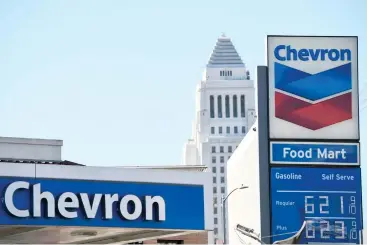  ?? ?? Los Angeles City Hall stands on the horizon as gasoline fuel prices above six dollars a gallon are displayed at a Chevron gas station.