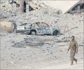  ?? AFP ?? A member of Syria's Arab Shaytat tribe who joined a Kurdish-led alliance fighting the Islamic State group in Syria, walks past the debris of a bombed car in the Syrian village of Baghouz.